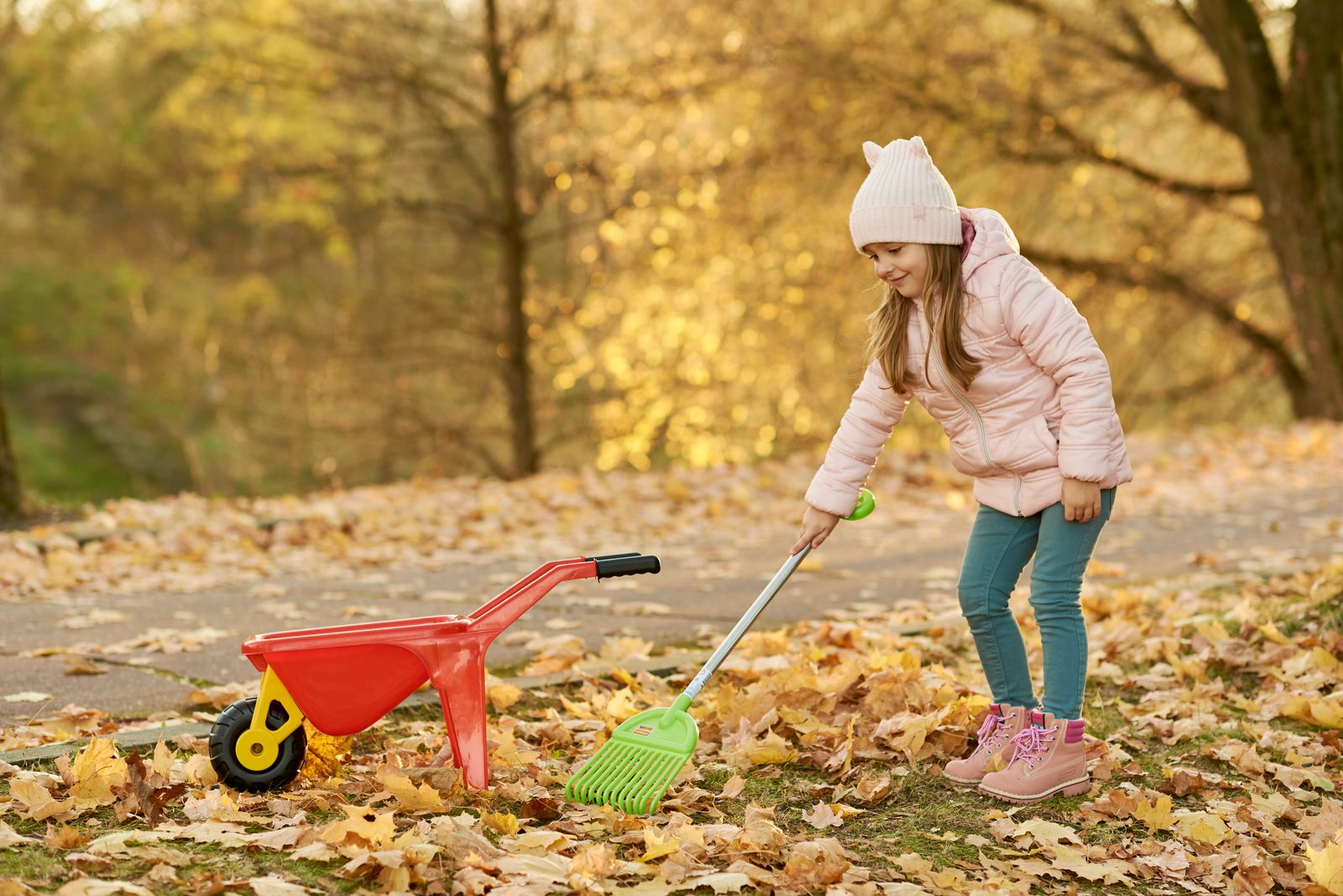 Kind hilft mit Rechen und Schubkarre im Garten